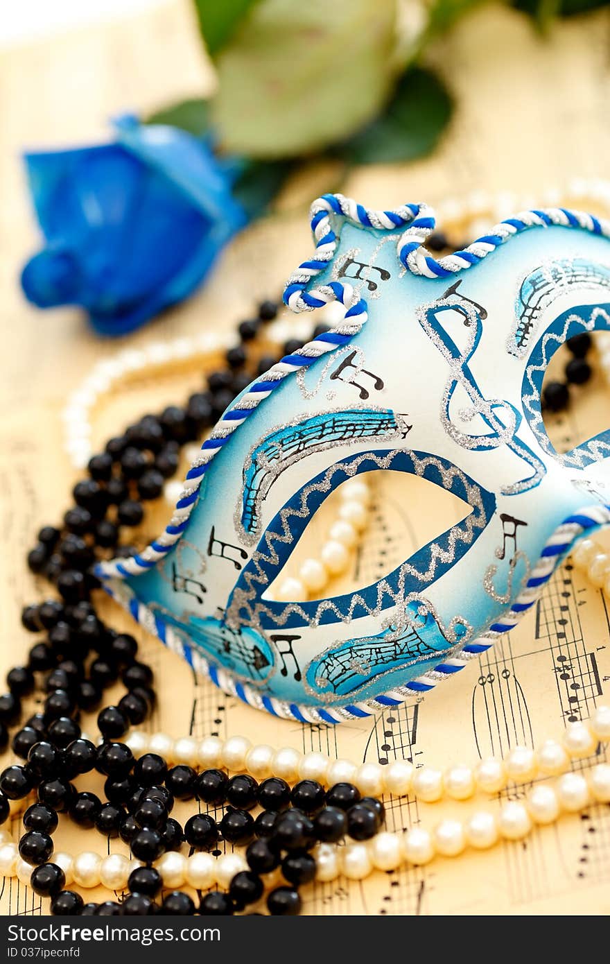 Ornate carnival mask on a music paper with rose, white and black pearls