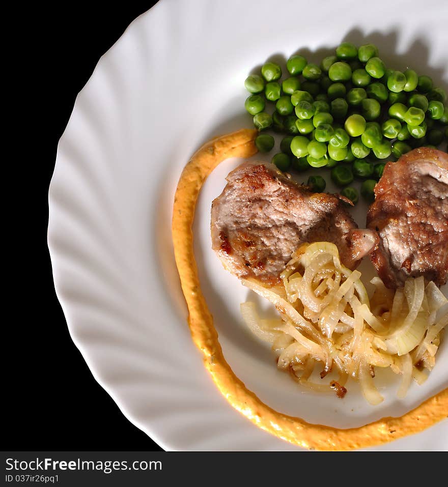 Fried meat (pork) with green peas on porcelain dish against black background. Fried meat (pork) with green peas on porcelain dish against black background