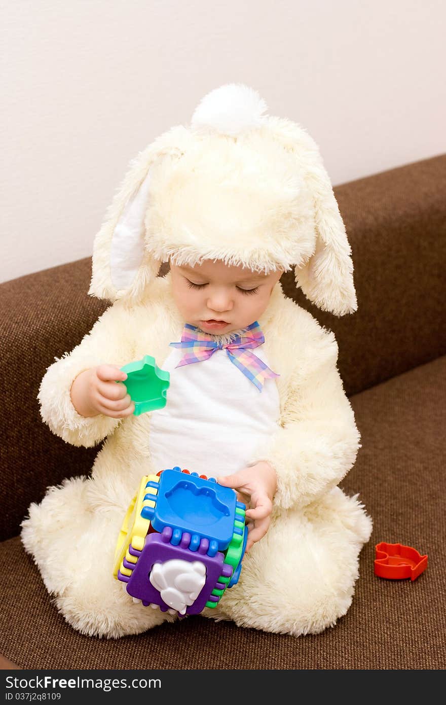 Pretty caucasian baby in rabbit costume playing with toy