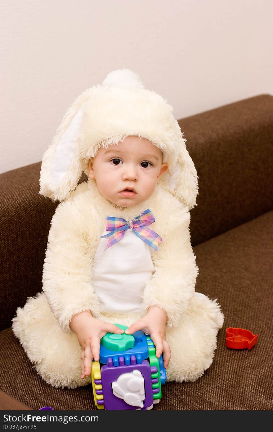 Pretty caucasian baby in rabbit costume playing with toy