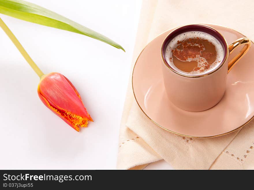 Cappuccino or espresso coffee in a cup with frothed milk and spring tulip flower on a white background