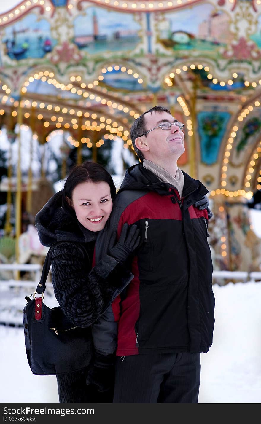 Happy couple looking at carousel in winter time