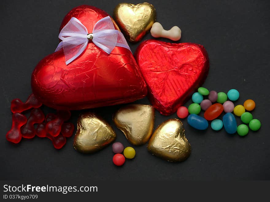 Two chocolate hearts covered with red shiny paper, one with a white silk bow, plus four small gold chocolate hearts and some candy. A gift for Valentine's Day. Two chocolate hearts covered with red shiny paper, one with a white silk bow, plus four small gold chocolate hearts and some candy. A gift for Valentine's Day.