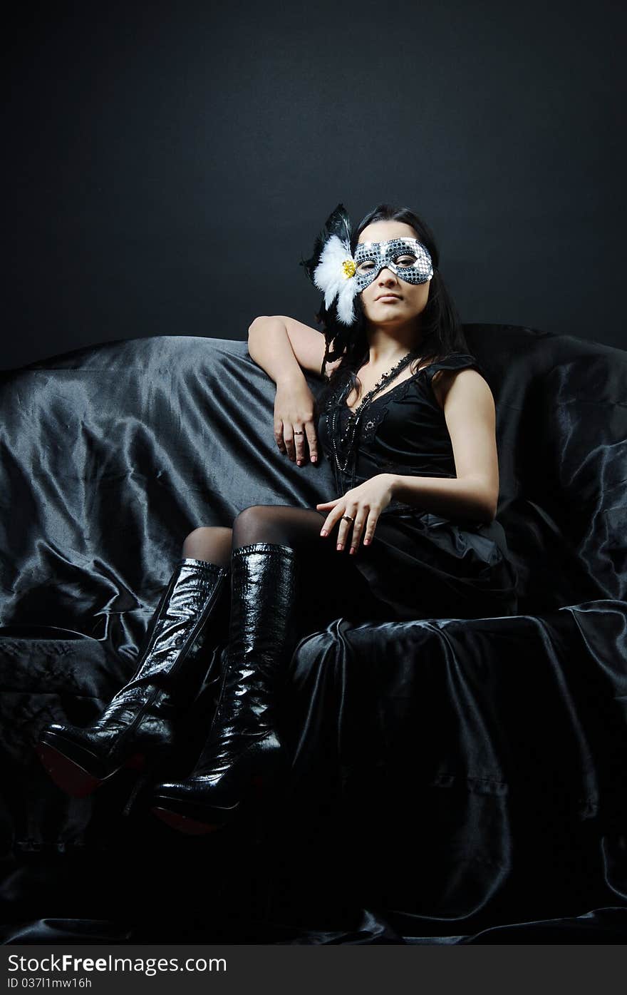 The girl sitting on a sofa on black silk in a mask. The girl sitting on a sofa on black silk in a mask