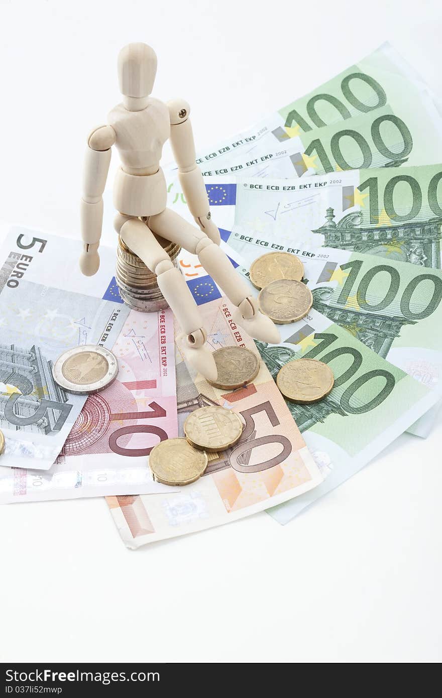 A wooden symbol figure sits on a stack of coins on banknotes. A wooden symbol figure sits on a stack of coins on banknotes