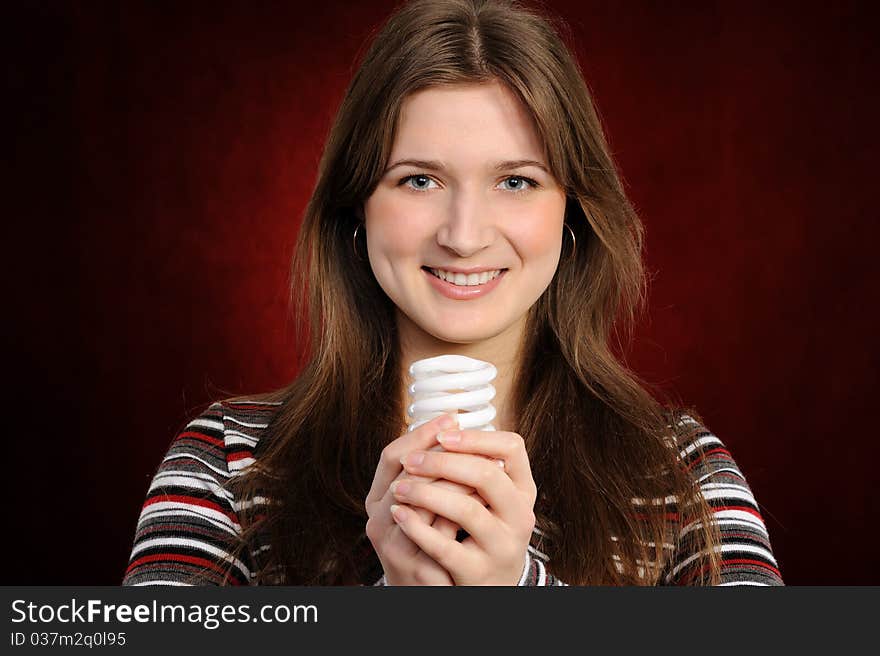 Young woman holding an fluorescent light bulb. On a red background