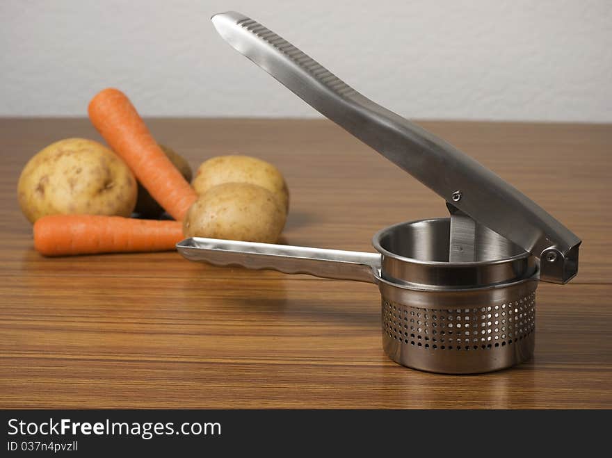 A horizontal image of a food ricer masher and vegetables on a wooden table. A horizontal image of a food ricer masher and vegetables on a wooden table