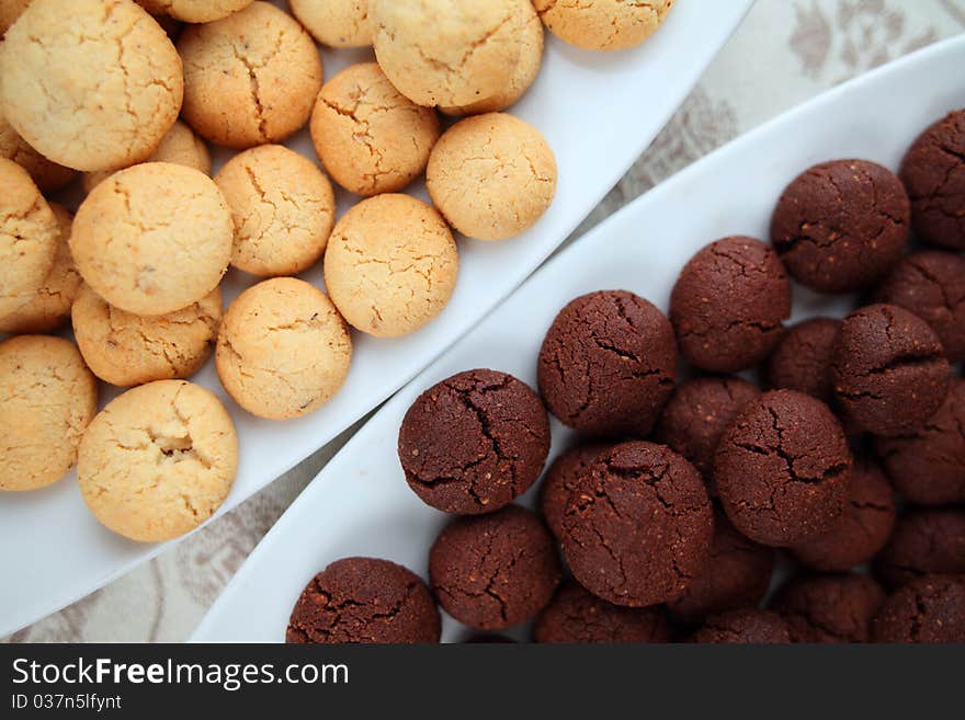 Black and vanilla home made cookies on plates over a damask tablecloth. Black and vanilla home made cookies on plates over a damask tablecloth