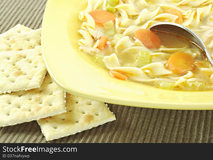 A bowl of hot homemade chicken noodle soup with crackers, horizontal with copy space