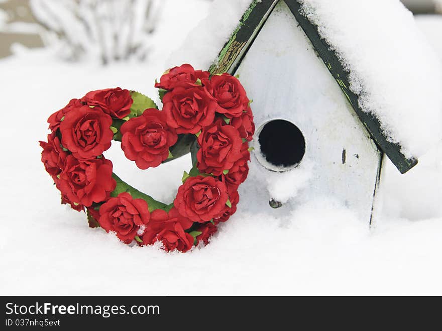 A red rose Valentine heart with a birdhouse in the snow, shallow depth of field with copy space. A red rose Valentine heart with a birdhouse in the snow, shallow depth of field with copy space