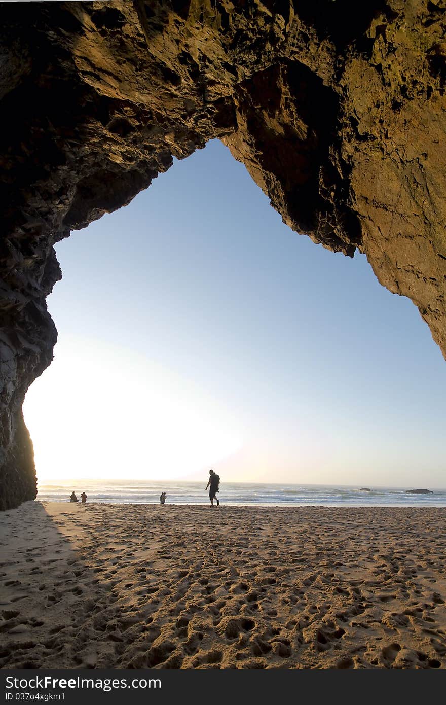 Tourist walking towards the, seen from a cave in the cliff. Tourist walking towards the, seen from a cave in the cliff