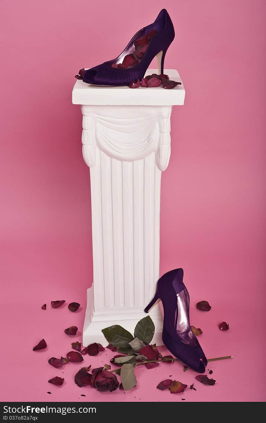 Purple high-heel shoes on pedestal with rose petals and a dying rose. Purple high-heel shoes on pedestal with rose petals and a dying rose