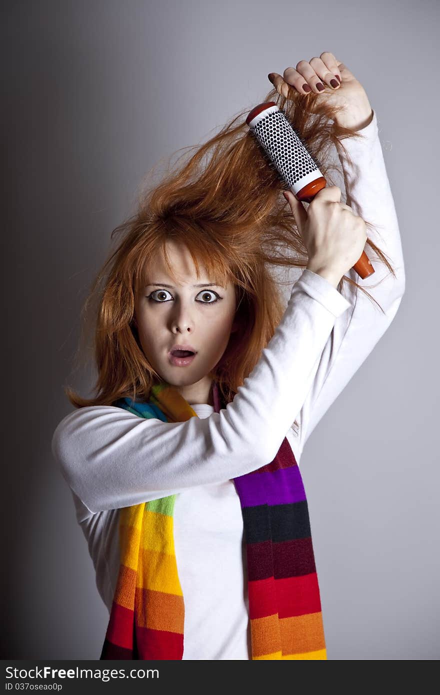 Sad red-haired girl with comb. Studio shot.