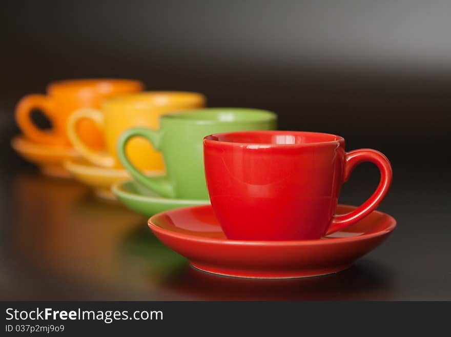 Four multi-colored ceramic cups are one after another on a black background. Four multi-colored ceramic cups are one after another on a black background