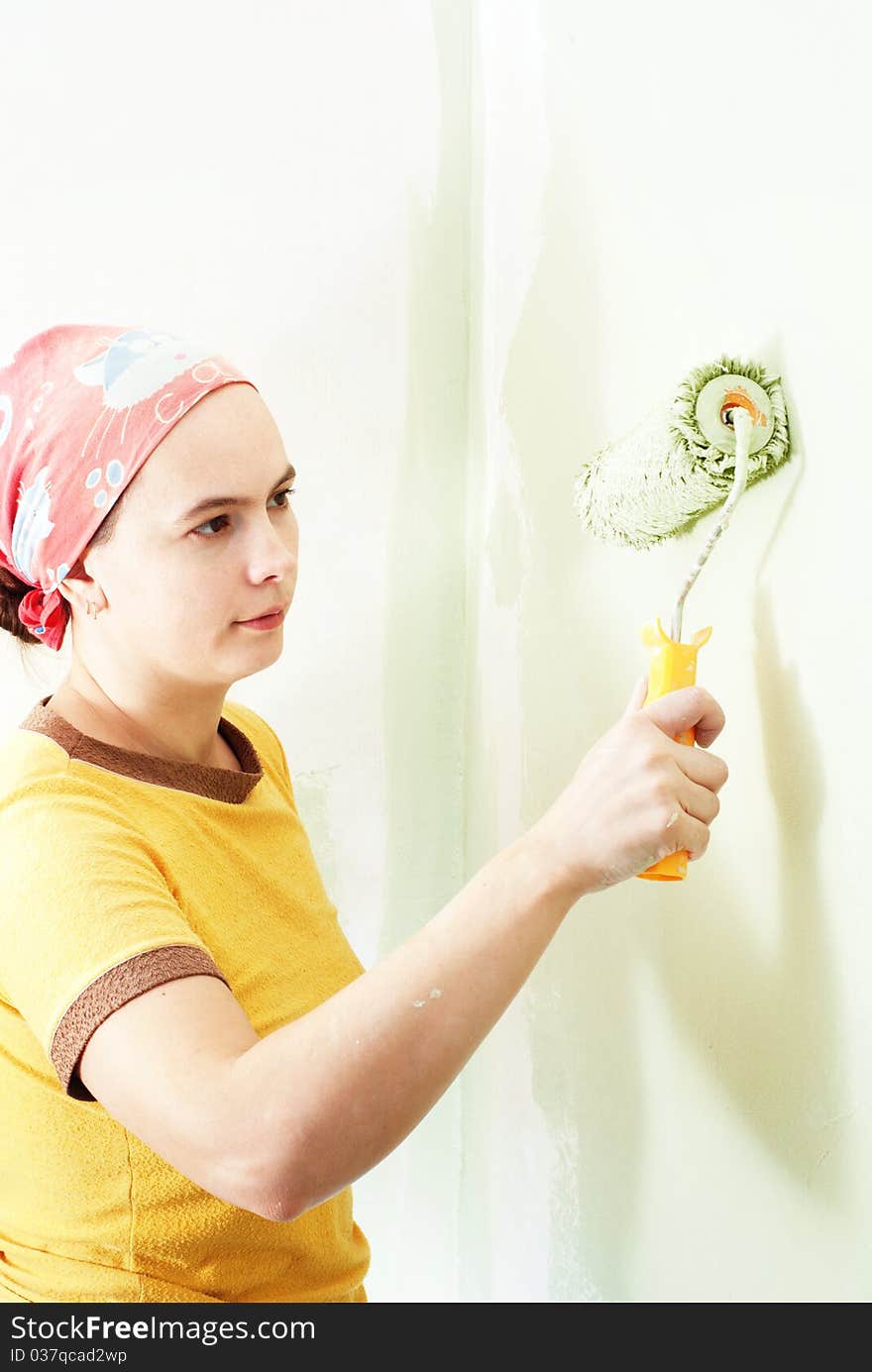 Young woman painting white wall with green paint. Young woman painting white wall with green paint