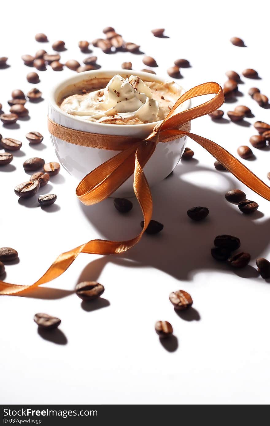 Cup of coffee with cream, coffee beans and golden ribbon