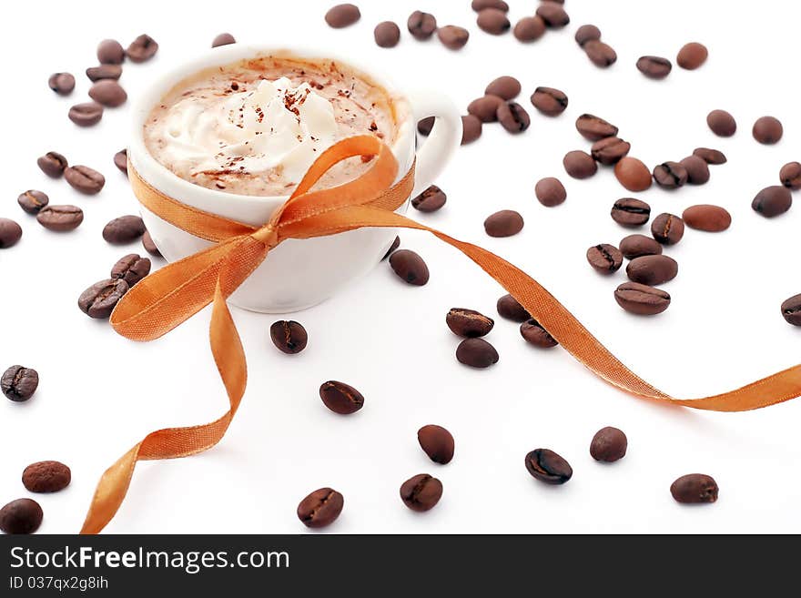 Cup of coffee with cream, coffee beans and golden ribbon