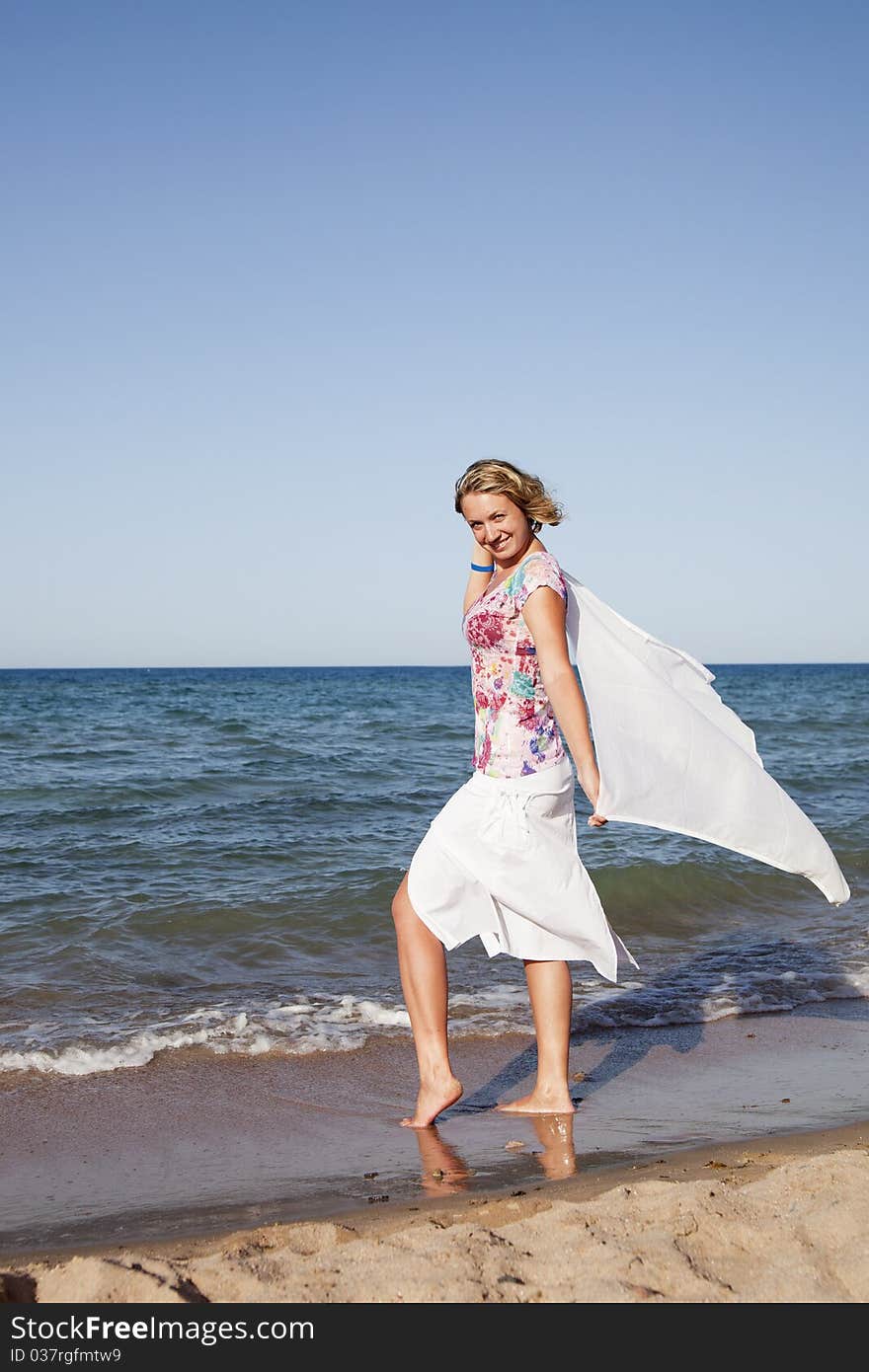 Beautiful girl standing with waving a scarf on the beach