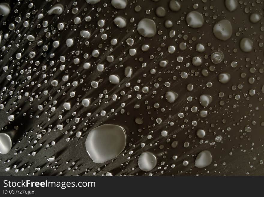 Water drops on a dark surface. The water droplets are very bright and contrast well with the dark background