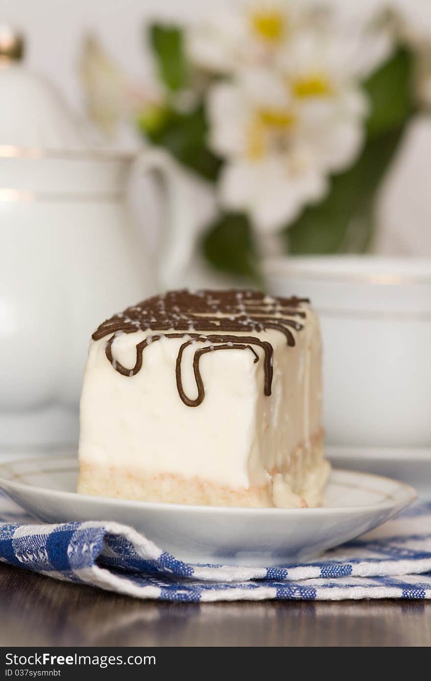 Dessert with icing and teapot on table against vase with flowers