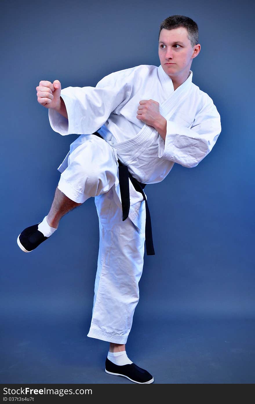 Young sporty karate man doing special exercise on gray background