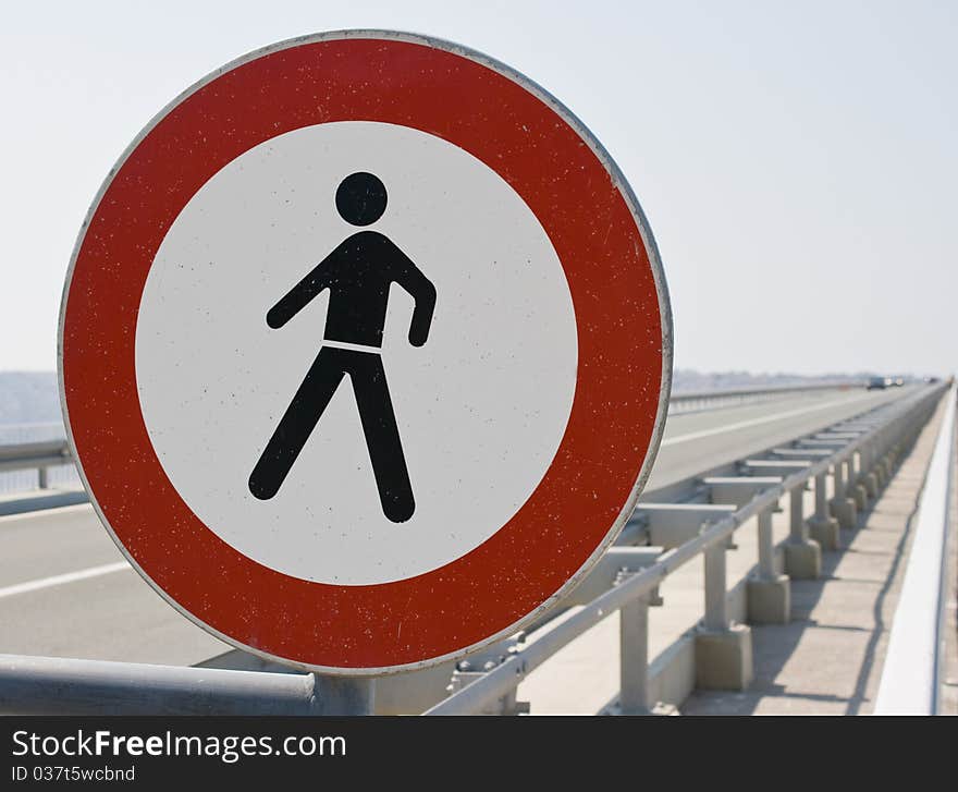 A damaged No trespassing sign at the side of the motorway. Defocused cars approaching.