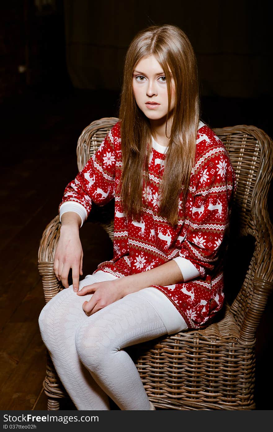 Cute woman sits in a chair wearing a sweater with the reindeer