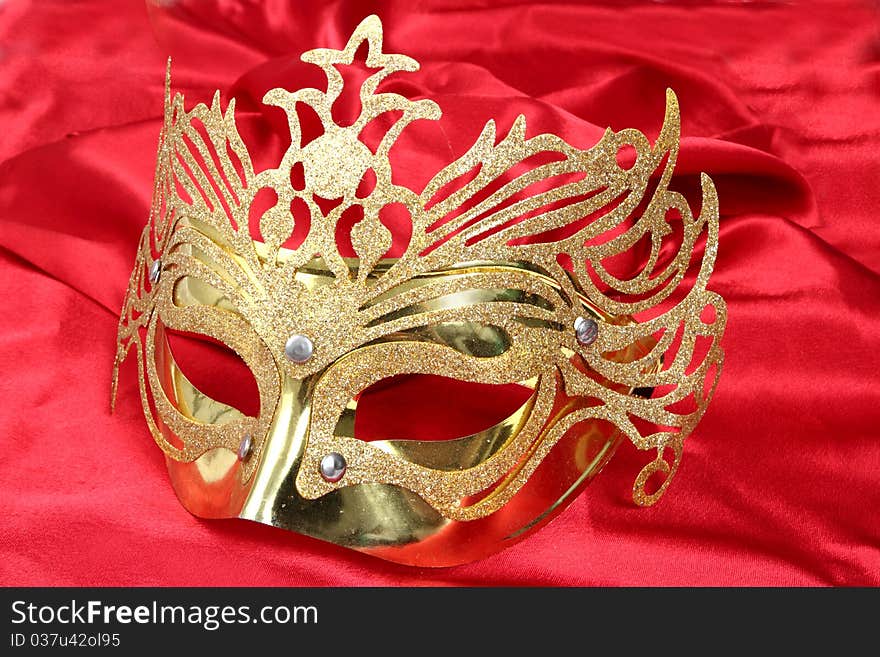 Gold mask with glitter on a satin red background. Gold mask with glitter on a satin red background