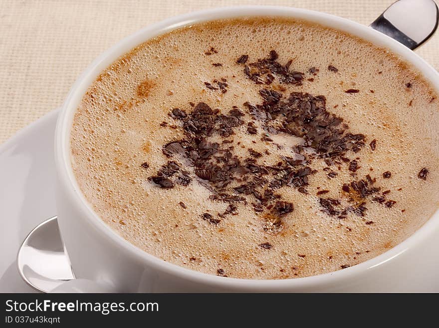 Cappuccino in a white ceramic cup with a saucer and a spoon.