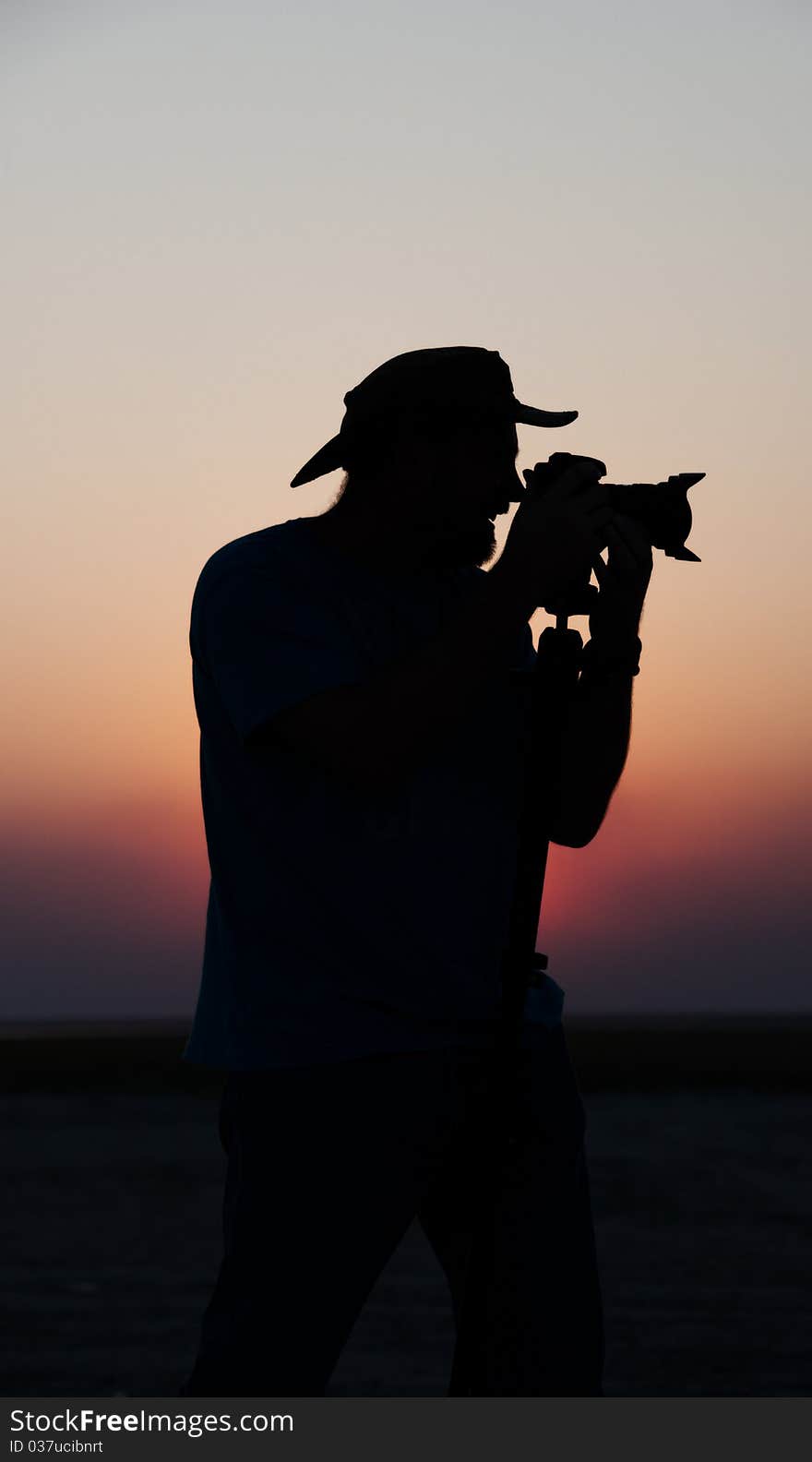 Silhouette of a young man in a hat taking pictures at sunset using a tripod. Silhouette of a young man in a hat taking pictures at sunset using a tripod