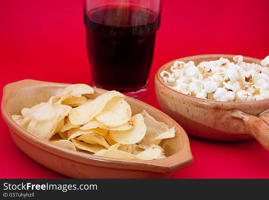 Tomato chips, pop corn and cola on red background