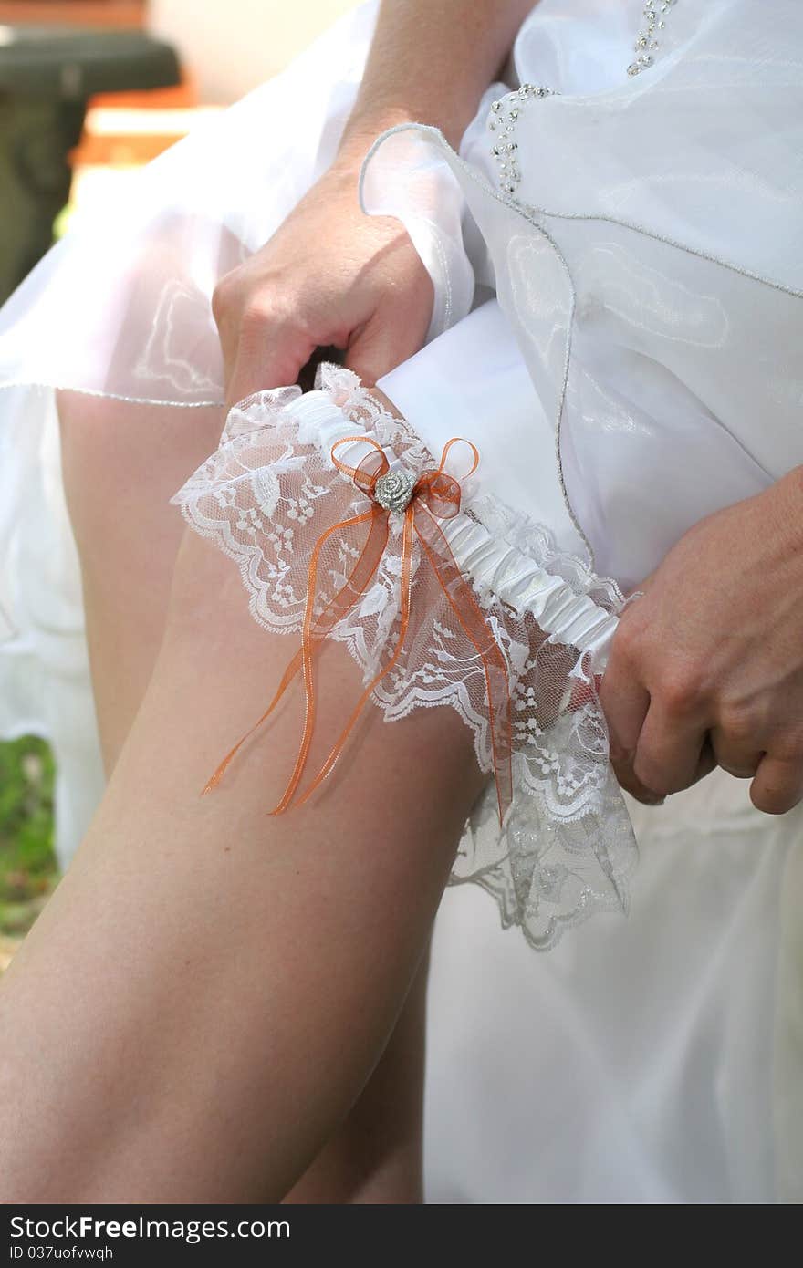 Bride in white wedding dress putting on her white and orange garter belt. Bride in white wedding dress putting on her white and orange garter belt