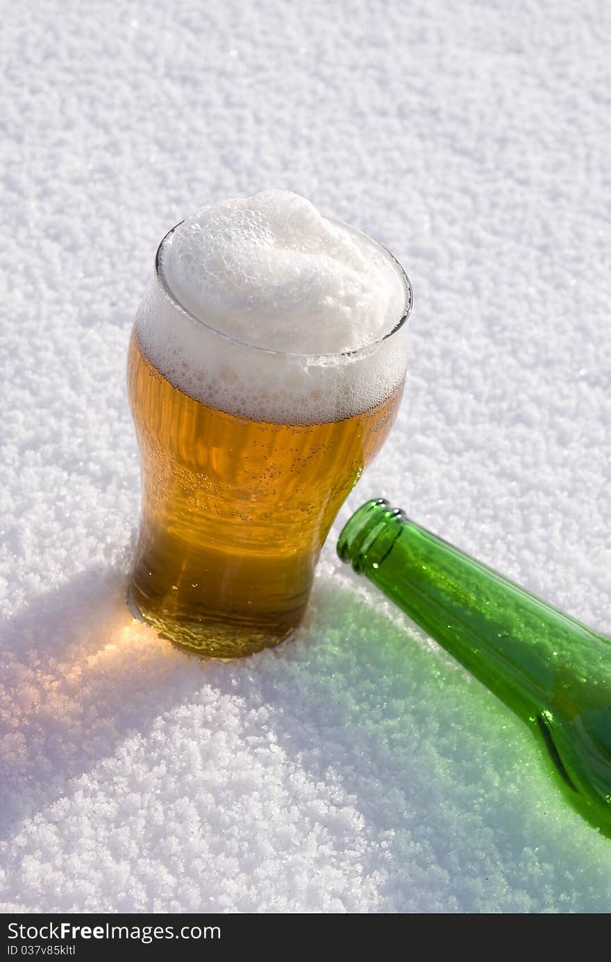 Beer in glass and green bottle on snow