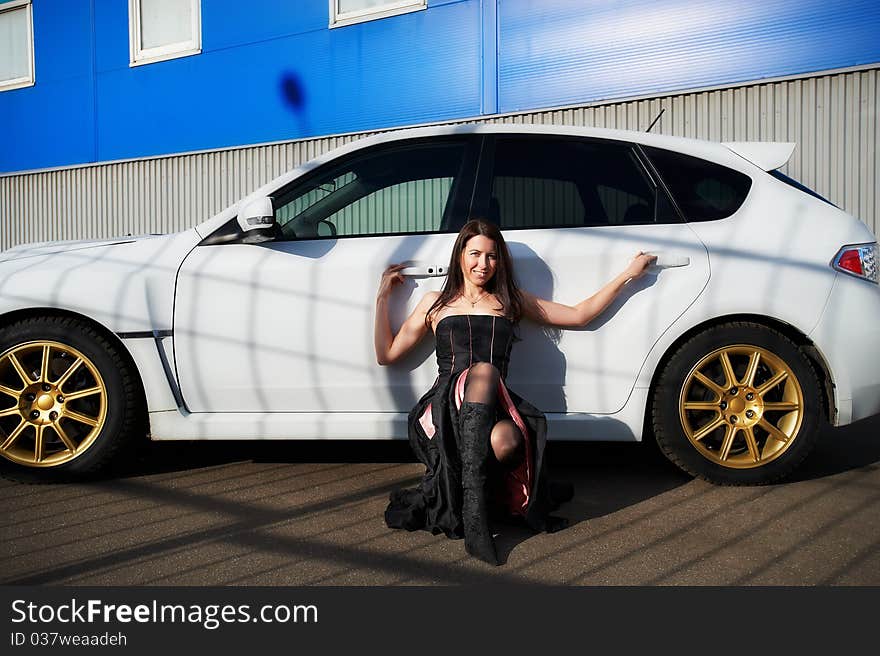 Young woman near white sports car on background industrial building