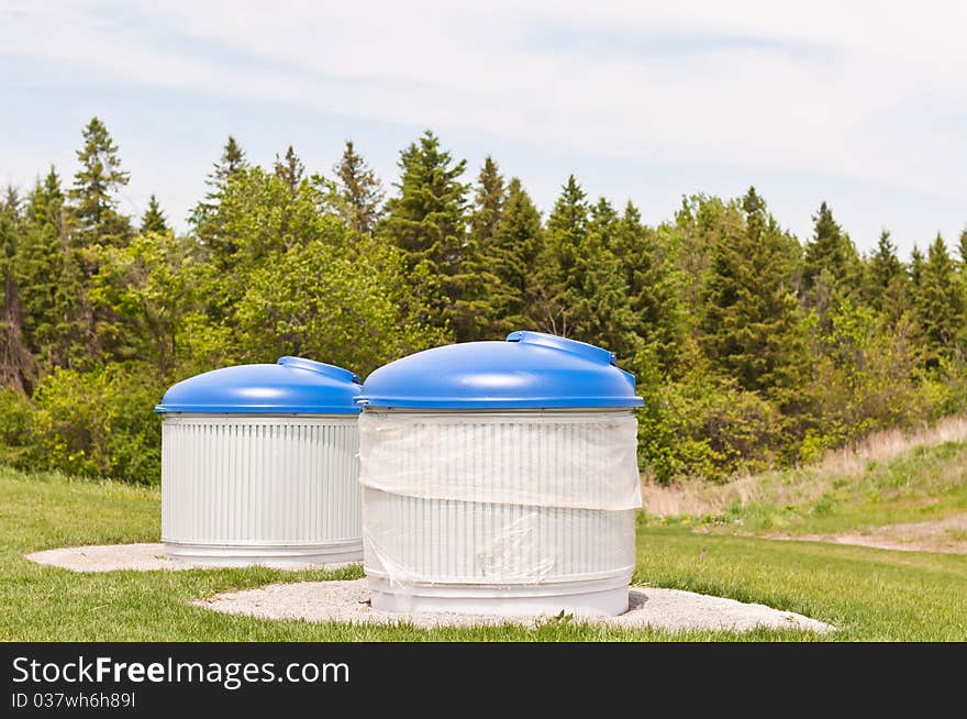 Large garbage and recycling bins sit outdoors in a park. Large garbage and recycling bins sit outdoors in a park.