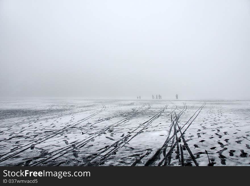 A distant cluster of people walking on melting ice on a lake in a dence winter fog. A distant cluster of people walking on melting ice on a lake in a dence winter fog