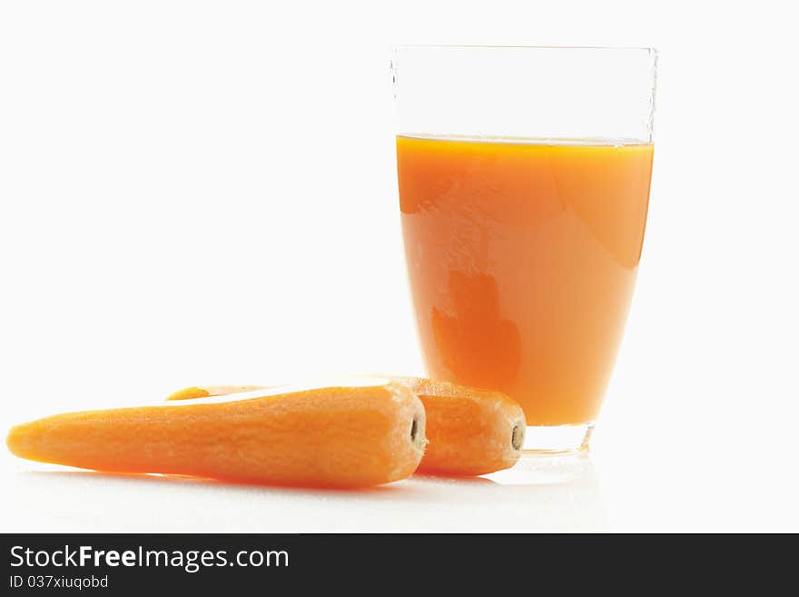 Two carrots close to a glass of fresh carrot juice