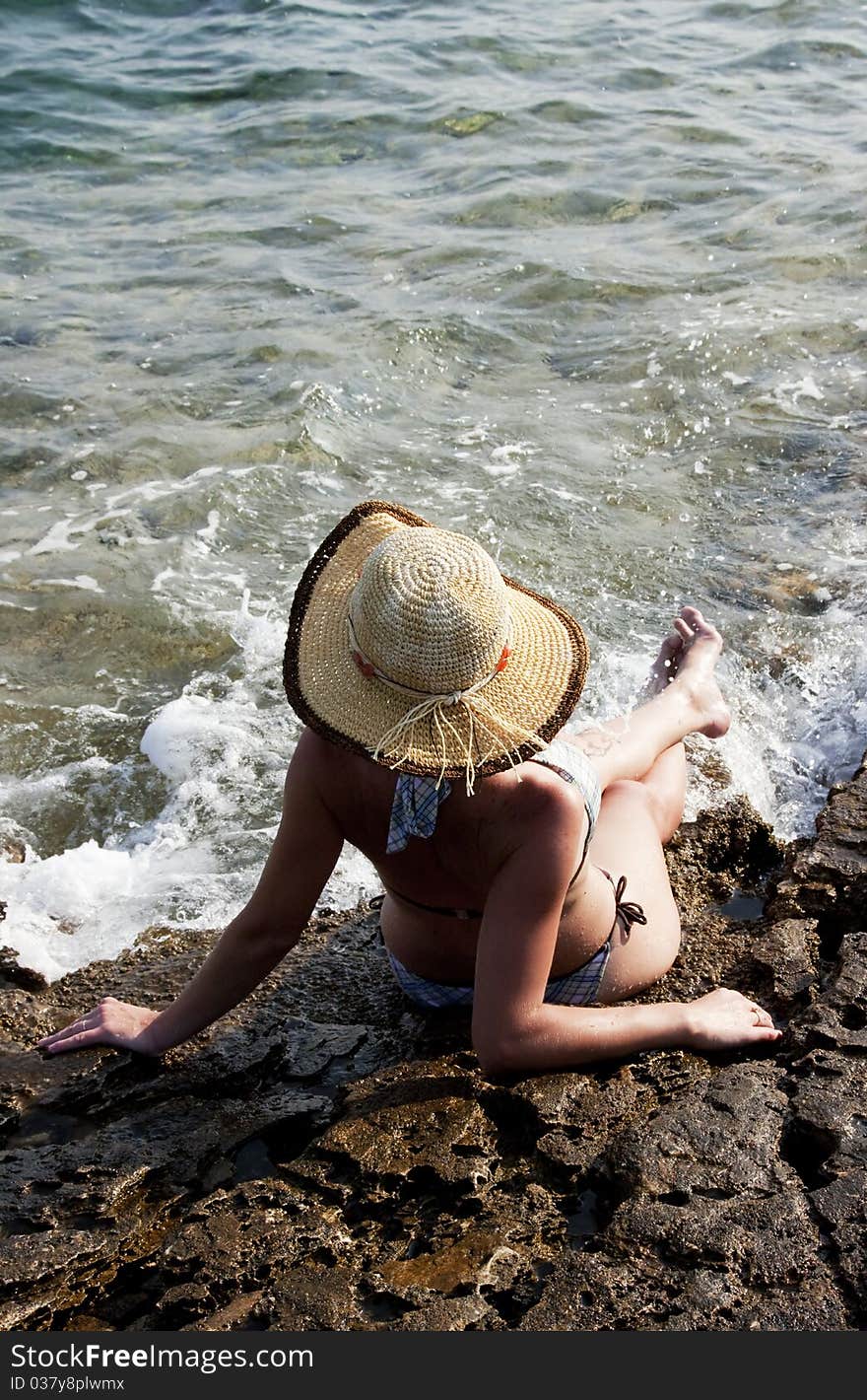 Woman with hat sunbathing on rocks