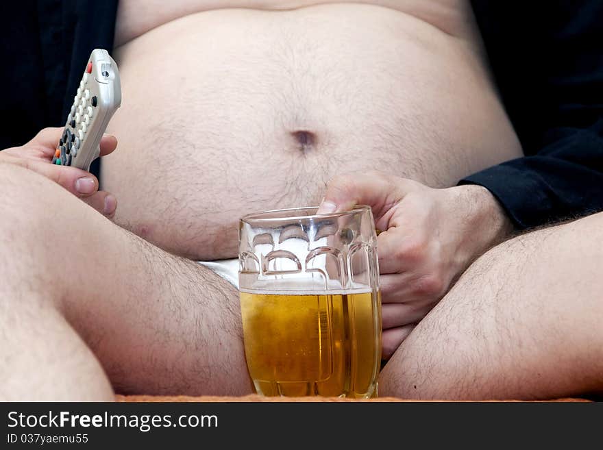 Overweight man sitting on the couch with a beer glass and remote control