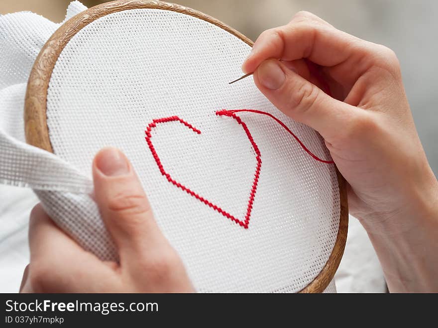 Female hands embroidering red heart. Female hands embroidering red heart