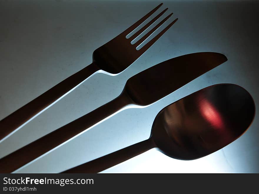 Close-up of eating set (knife, fork and spoon) in smooth red light against grey background. Close-up of eating set (knife, fork and spoon) in smooth red light against grey background.