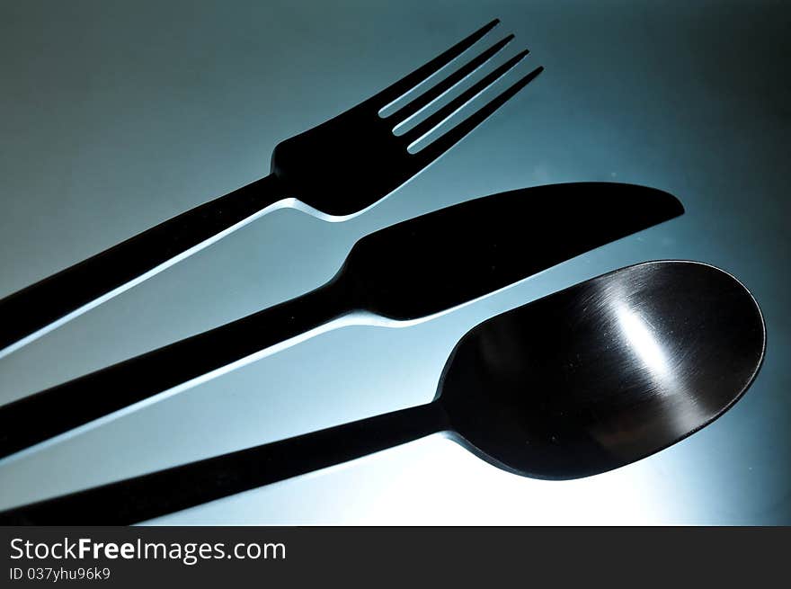 Close-up of eating set (knife, fork and spoon) in smooth white light against light blue background. Close-up of eating set (knife, fork and spoon) in smooth white light against light blue background.