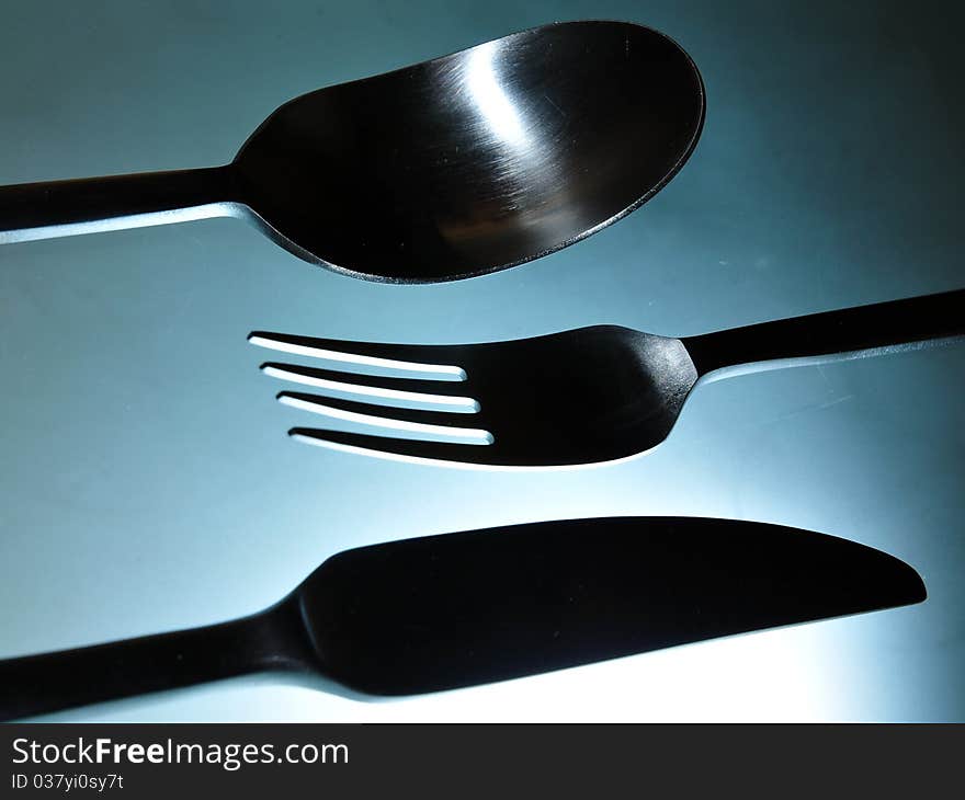 Close-up of eating set (knife, fork and spoon) in smooth white light against light blue background. Close-up of eating set (knife, fork and spoon) in smooth white light against light blue background.