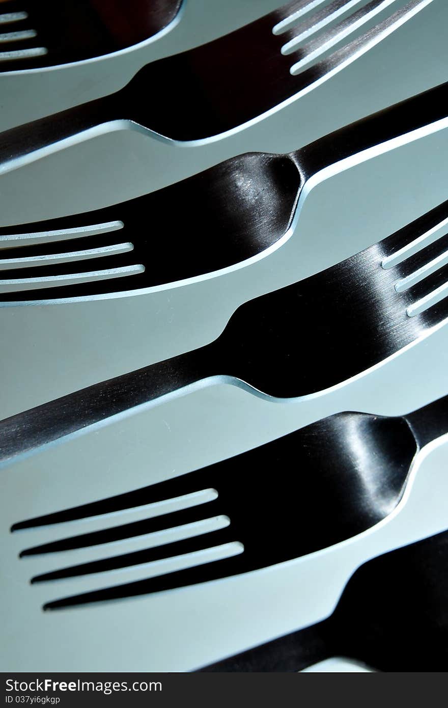 Close-up of six stainless steel eating forks in smooth white light against light blue background.