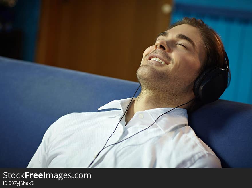 Caucasian adult man relaxing on sofa with headphones. Horizontal shape, side view, head and shoulders, copy space. Caucasian adult man relaxing on sofa with headphones. Horizontal shape, side view, head and shoulders, copy space