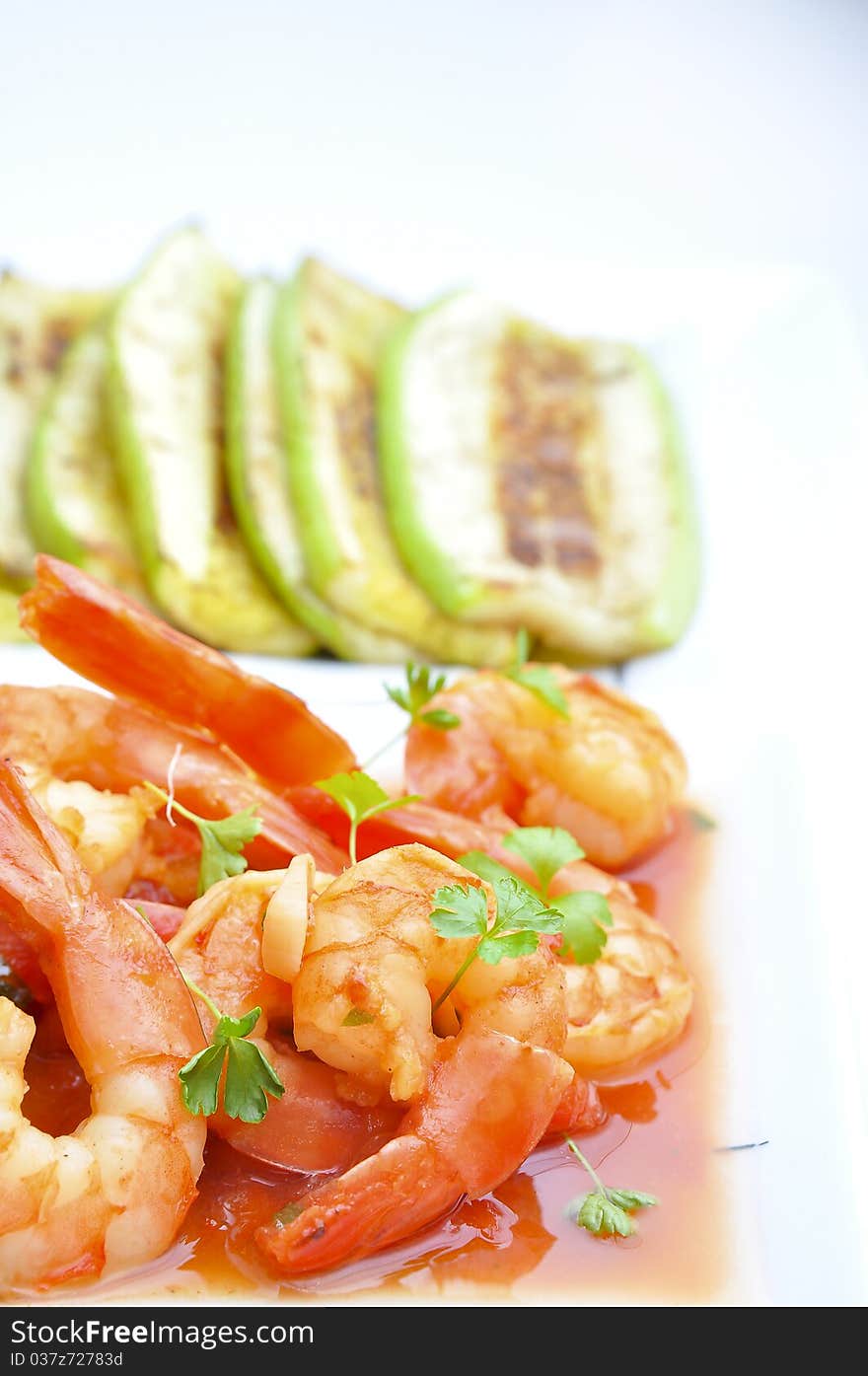 Shrimps in tomato sauce with rice and zuchinni on white plate and background.