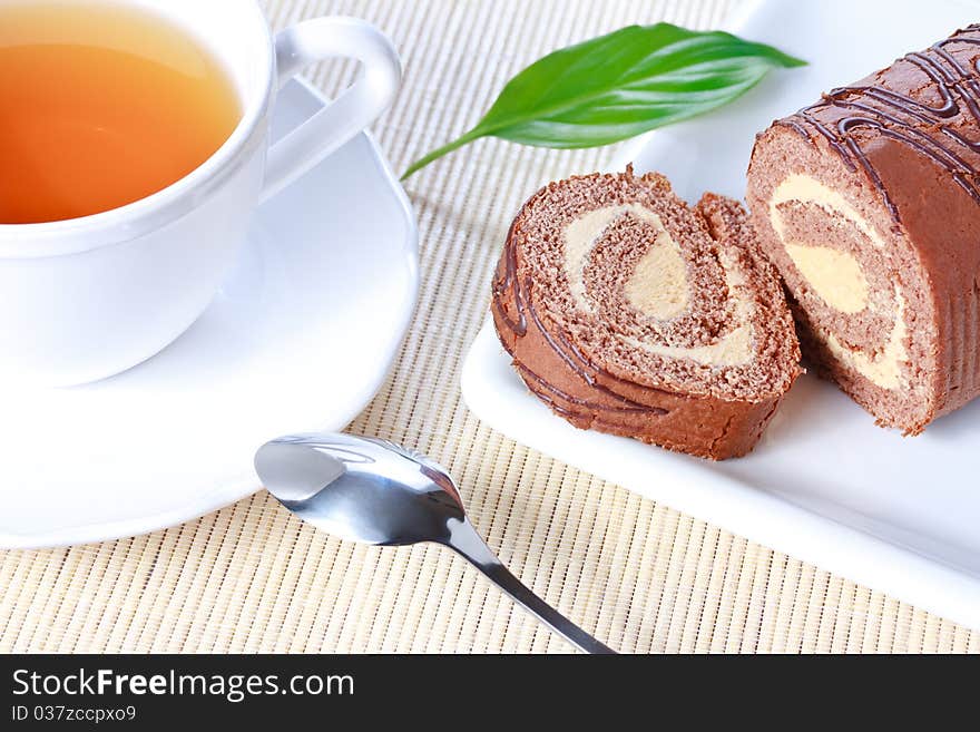 Closeup swiss roll with condensed milk cream on white plate and a cup of tea. Closeup swiss roll with condensed milk cream on white plate and a cup of tea