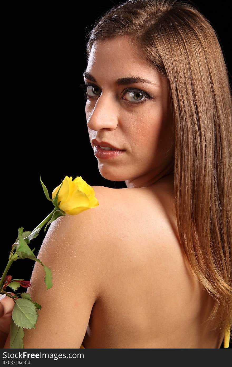 Portrait of beautiful young caucasion woman holding single yellow rose. Model has back to camera and looking back over a naked shoulder. Portrait of beautiful young caucasion woman holding single yellow rose. Model has back to camera and looking back over a naked shoulder.