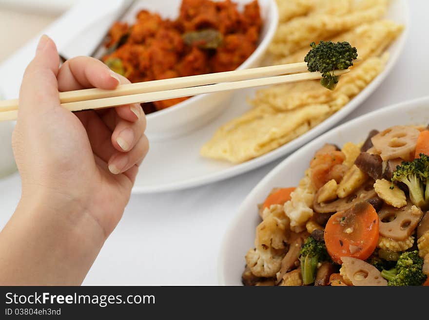 A woman holds a broccoli with chopsticks. A woman holds a broccoli with chopsticks