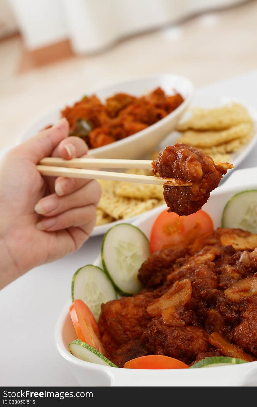 A woman holding a piece of chicken meat with chopsticks. A woman holding a piece of chicken meat with chopsticks